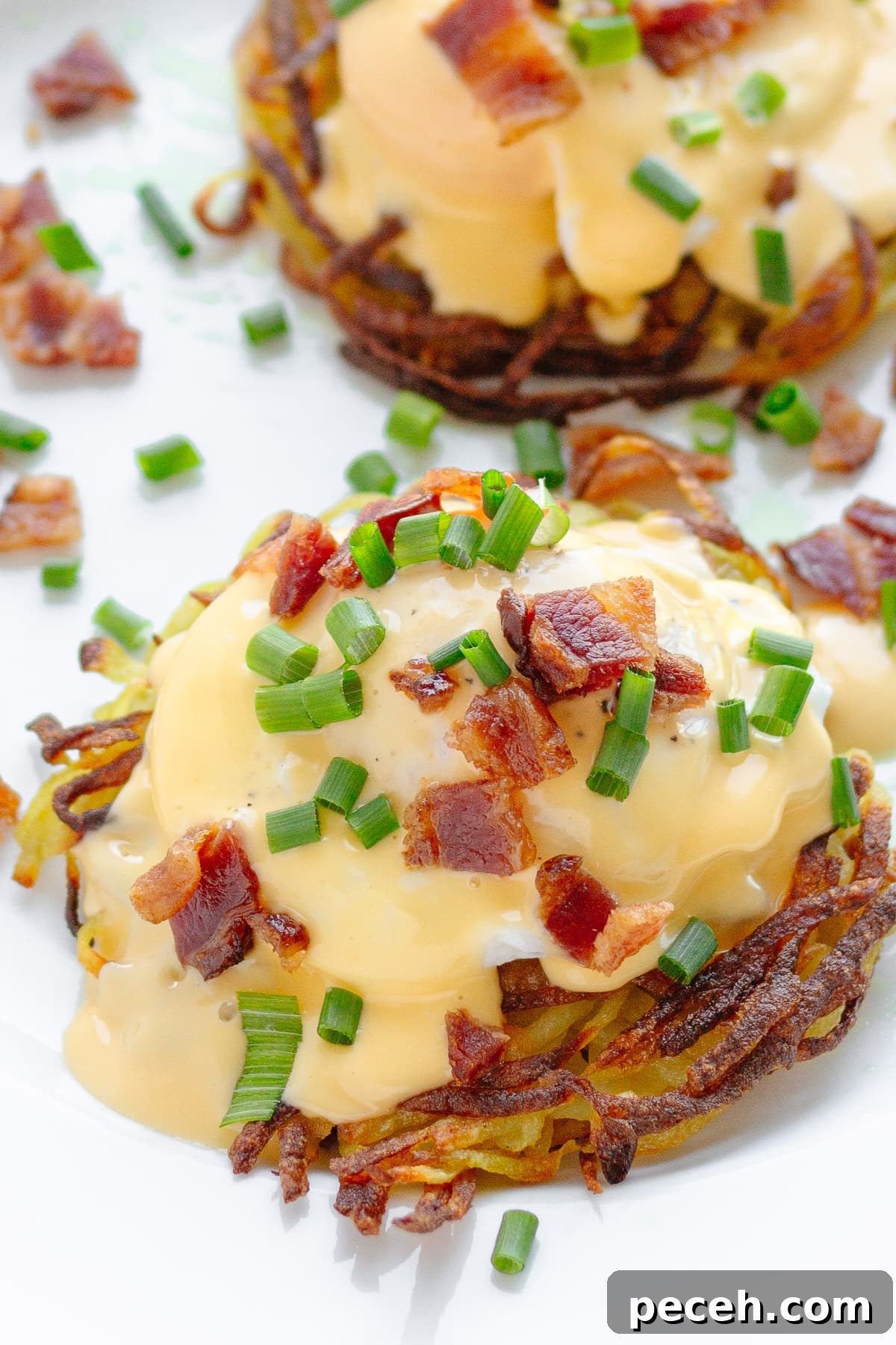 Rösti Eggs Benedict with Crispy Potato Cakes 3 Two Rosti Eggs Benedict on a white plate garnished with chopped bacon and fresh chives.