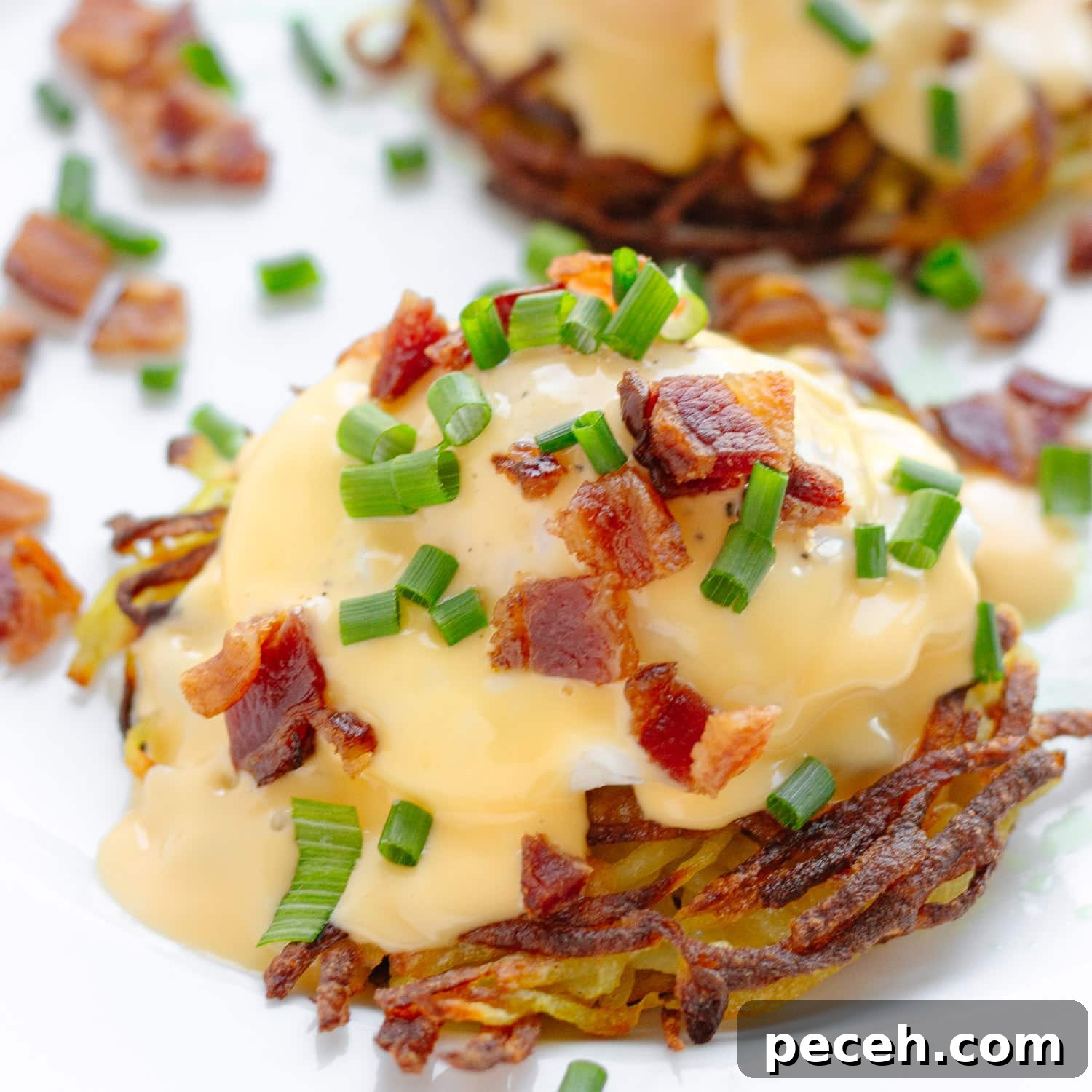 Rösti Eggs Benedict with Crispy Potato Cakes 7 Closeup of eggs Benedict on a potato rosti garnished with chopped bacon and chives.