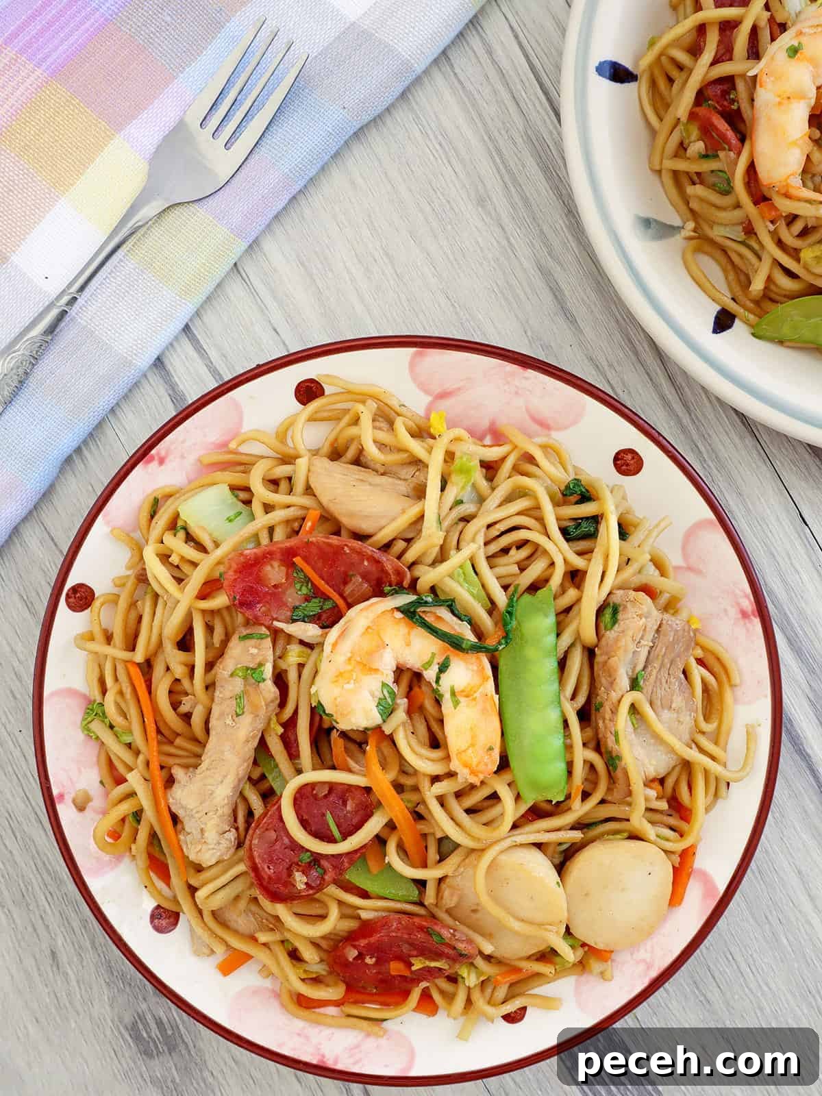 Filipino pancit canton guisado with shrimp, sausage, and veggies on a plate