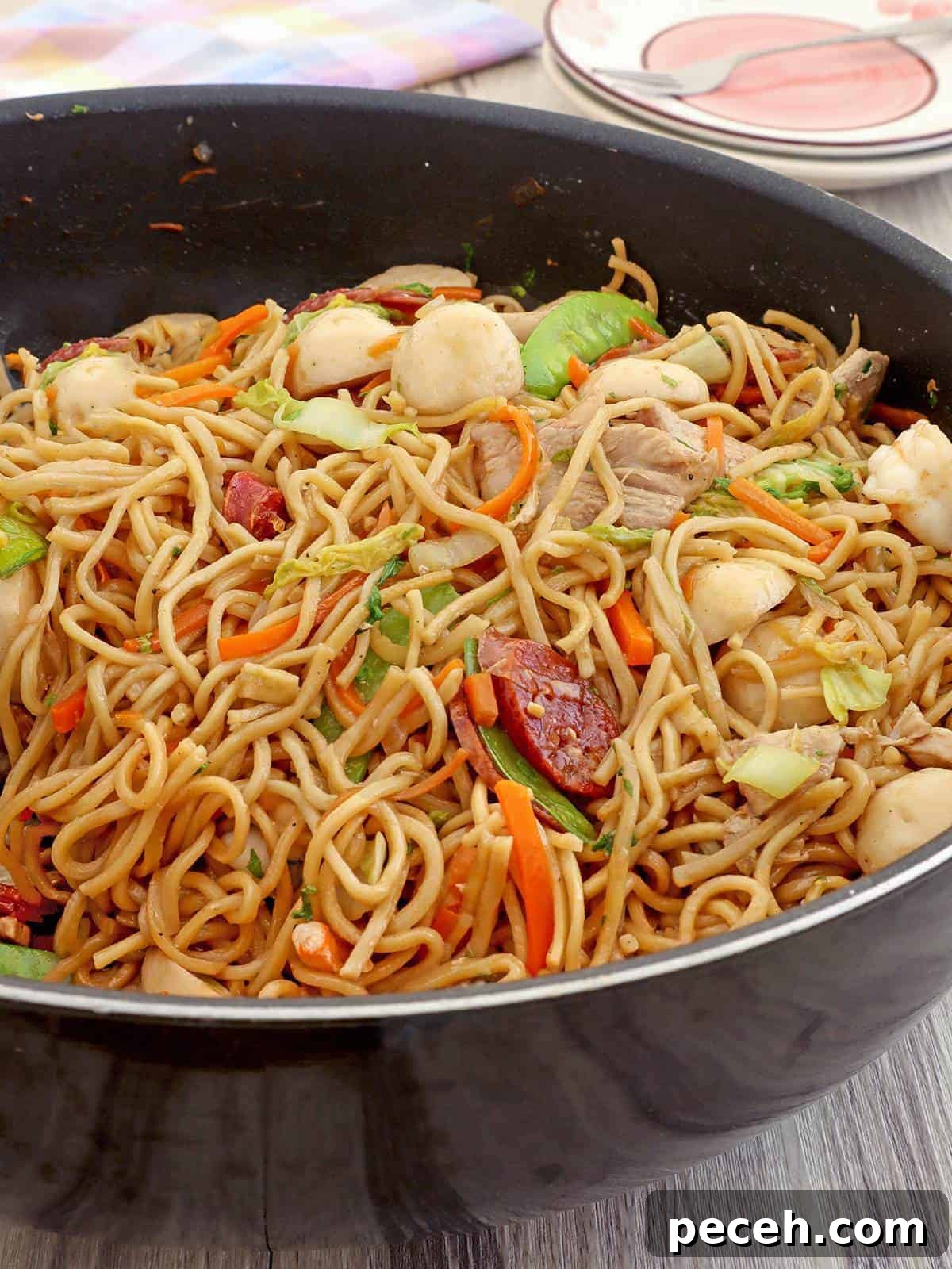Pancit canton Guisado with fish balls, sausage, snow peas, carrots, cabbage n a wok