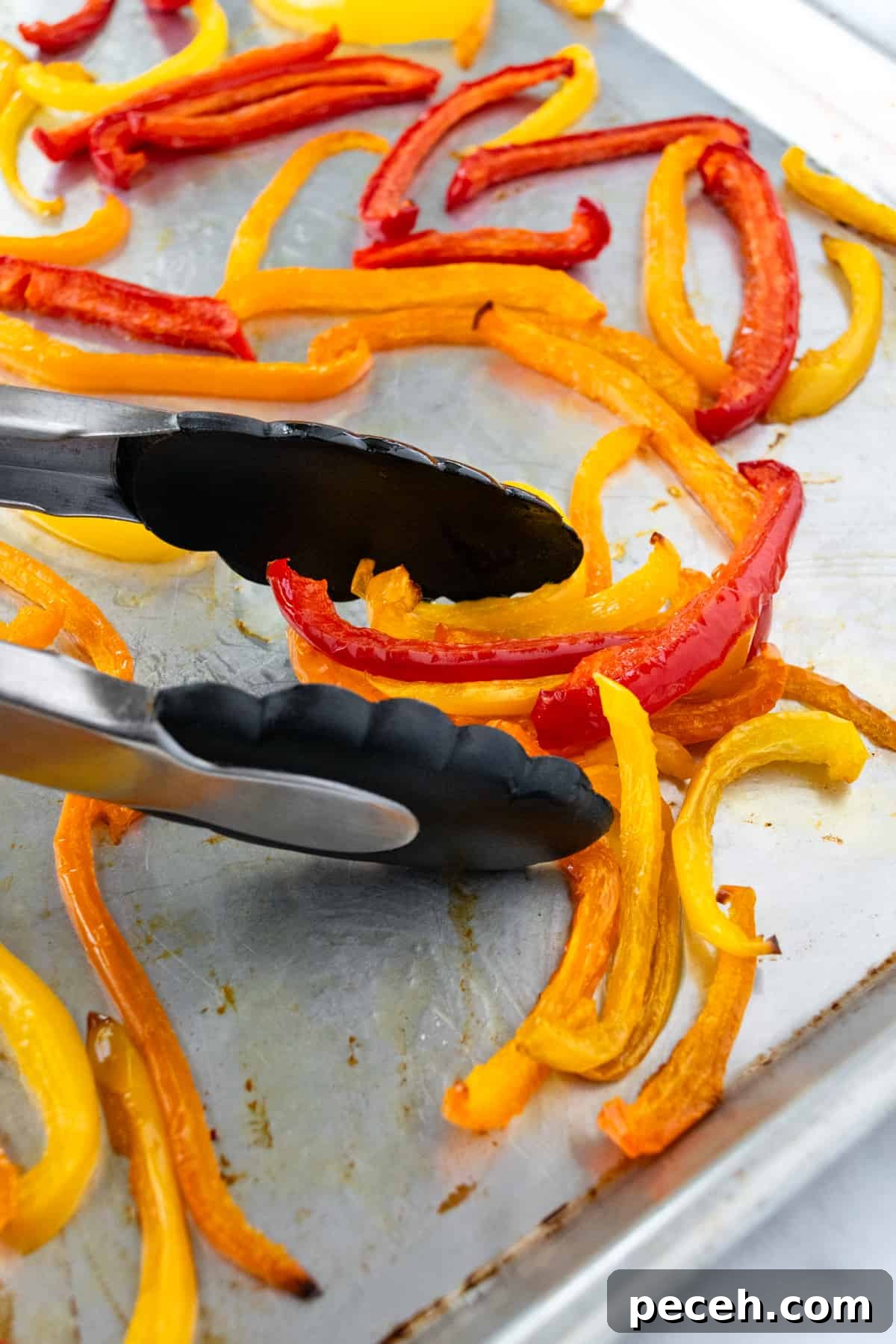 Tongs grabbing roasted bell pepper slices from a baking sheet.