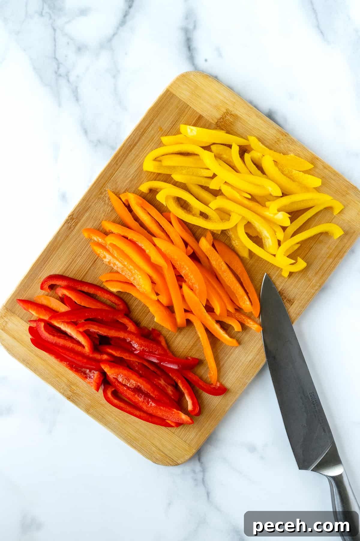 Sliced red, orange, and yellow bell peppers on a cutting board with a knife.