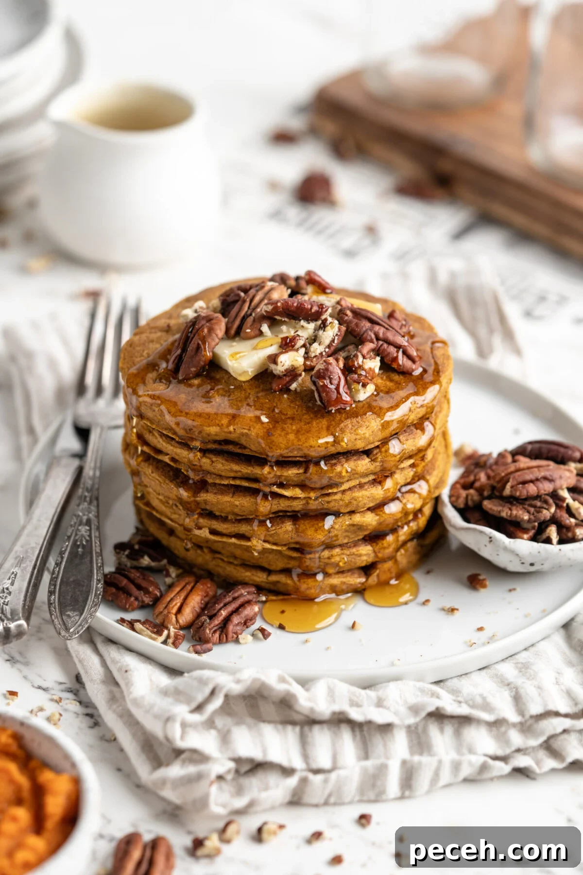 Fluffy vegan pumpkin pancakes are easy to make and loaded with your favorite warm spices. Perfect for a cozy fall breakfast or family brunch! Overhead view of a stack of pumpkin pancakes on a plate, topped with nuts, next to a bowl of nuts and a fork.