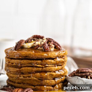 Fluffy Pumpkin Pancake Recipe for Fall Breakfast 2 A stack of pumpkin pancakes on a plate, topped with nuts, next to a bowl of nuts.