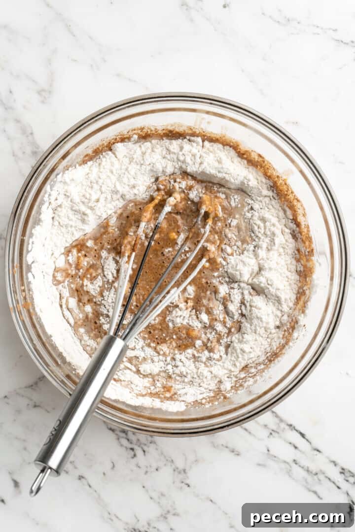 Add the dry ingredients. Overhead view of a mixing bowl with a whisk mixing flour into almond milk and pumpkin puree.