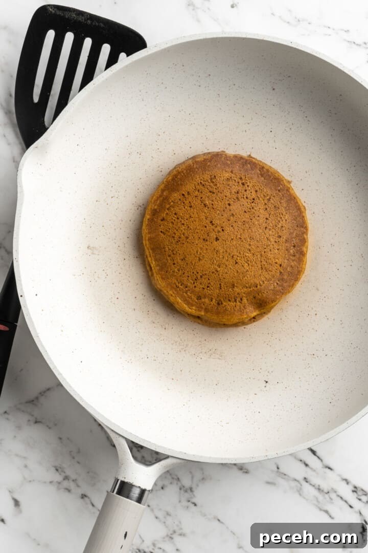 Flip, and repeat. Overhead view of a cooked pumpkin pancake in a pan.