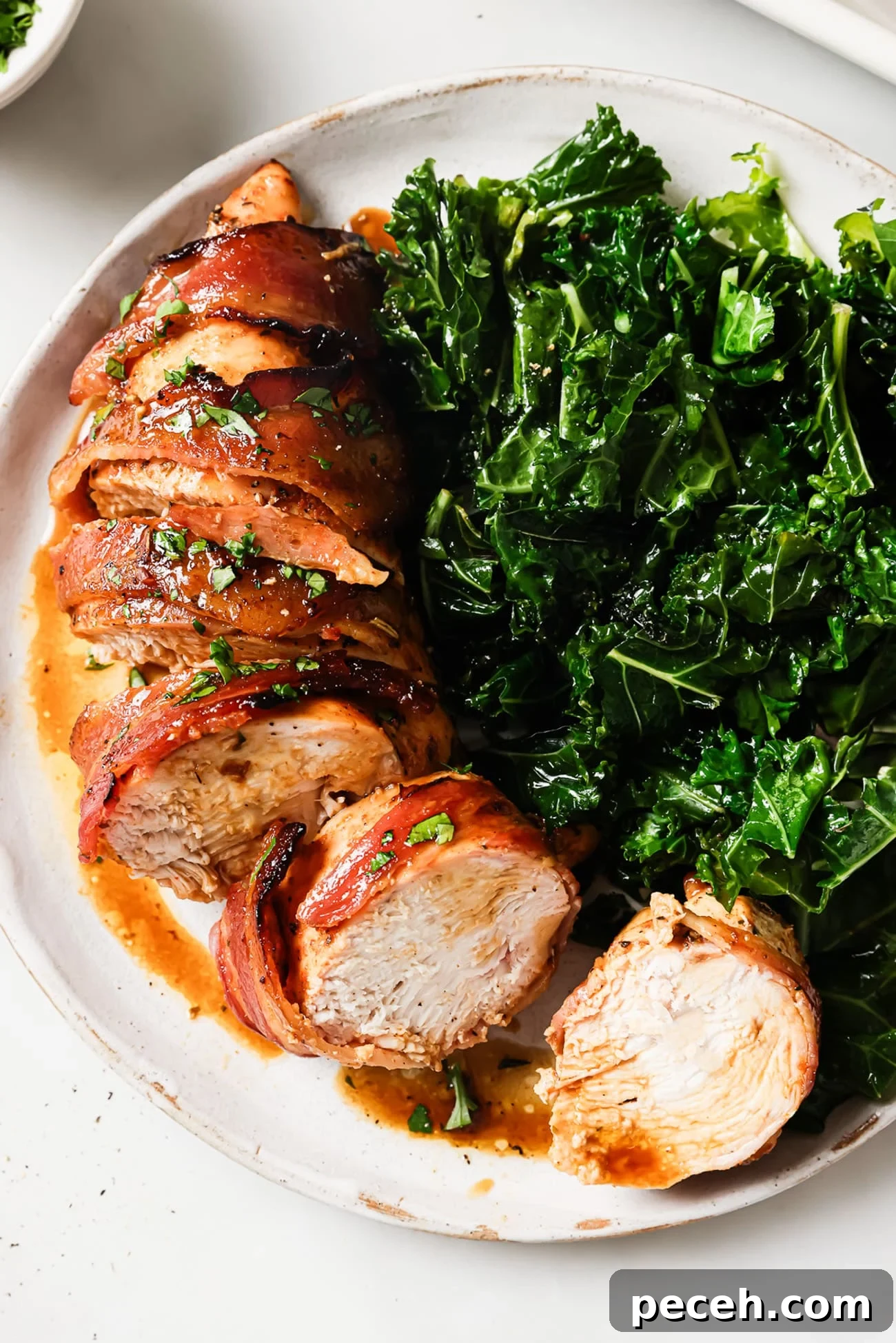Juicy Bacon-Wrapped Chicken Breast Recipe for Dinner 2 A sliced bacon-wrapped chicken breast next to a side of wilted kale on a white plate.