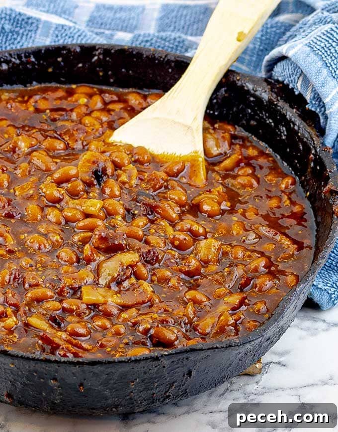 Bourbon Bacon Grilled Baked Beans in a cast iron skillet with a wooden spoon and blue towel