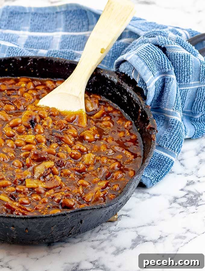 Bourbon Bacon Grilled Baked Beans in a cast iron skillet with a wooden spoon and blue towel