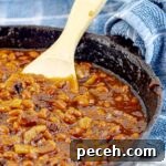 Bourbon Bacon Grilled Baked Beans in a cast iron skillet with a wooden spoon and blue towel