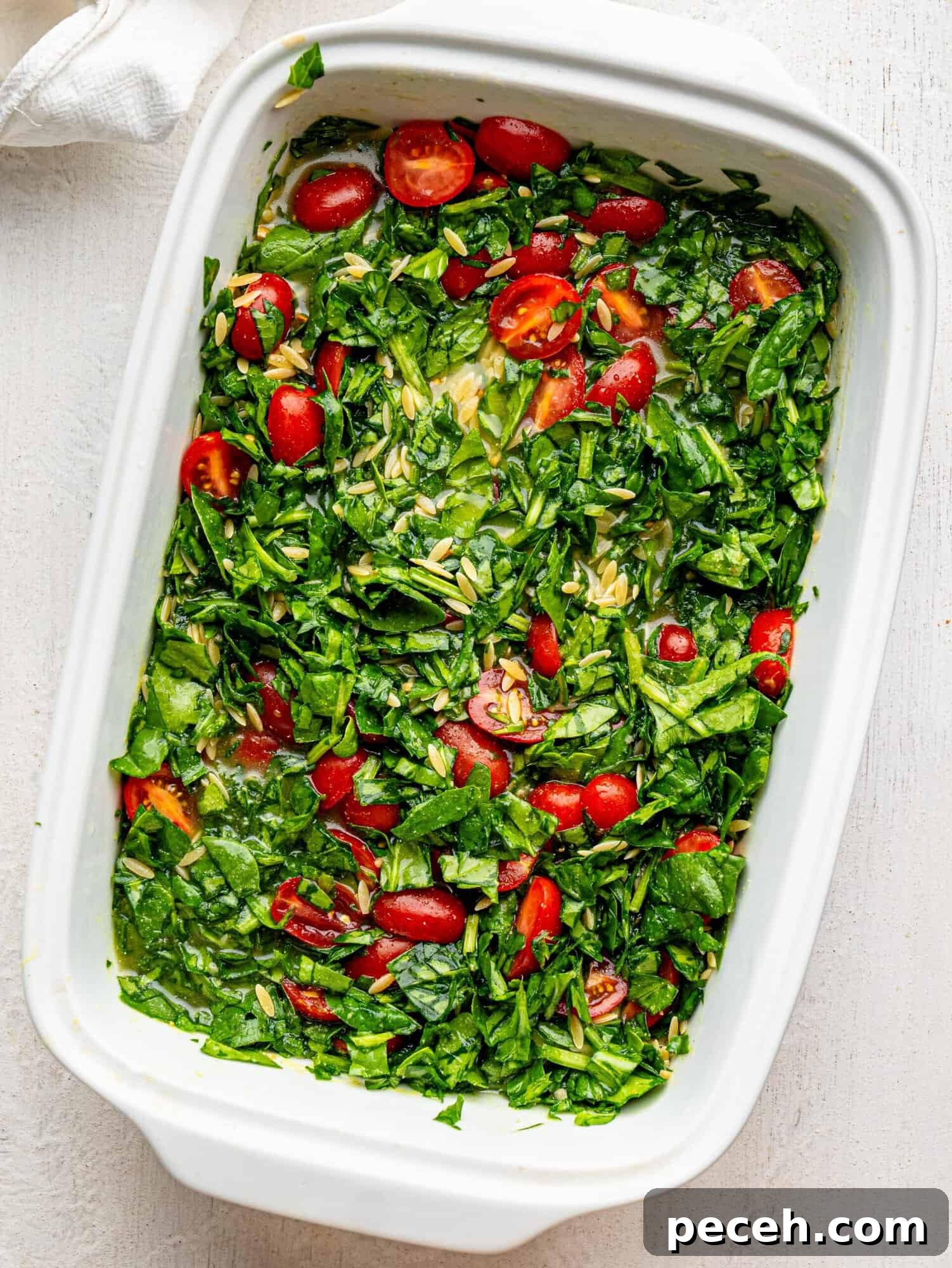 Spinach, Feta & Chicken Orzo Bake — Cheesy One-Pan Dinner 10 Orzo with feta, spinach and tomatoes in a white casserole dish before baking.