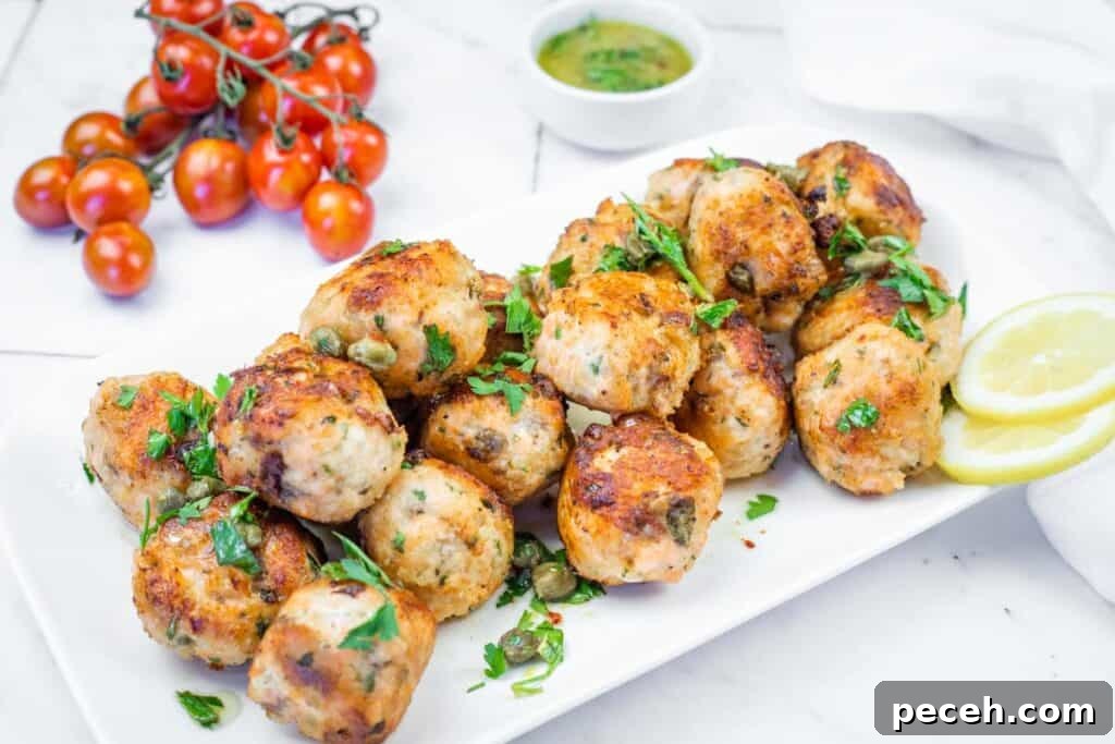 Crispy Pan-Fried Salmon Balls with Tangy Dill Sauce 14 A white platter filled with golden-brown chicken meatballs, garnished with parsley and capers, served with lemon slices and a green sauce.