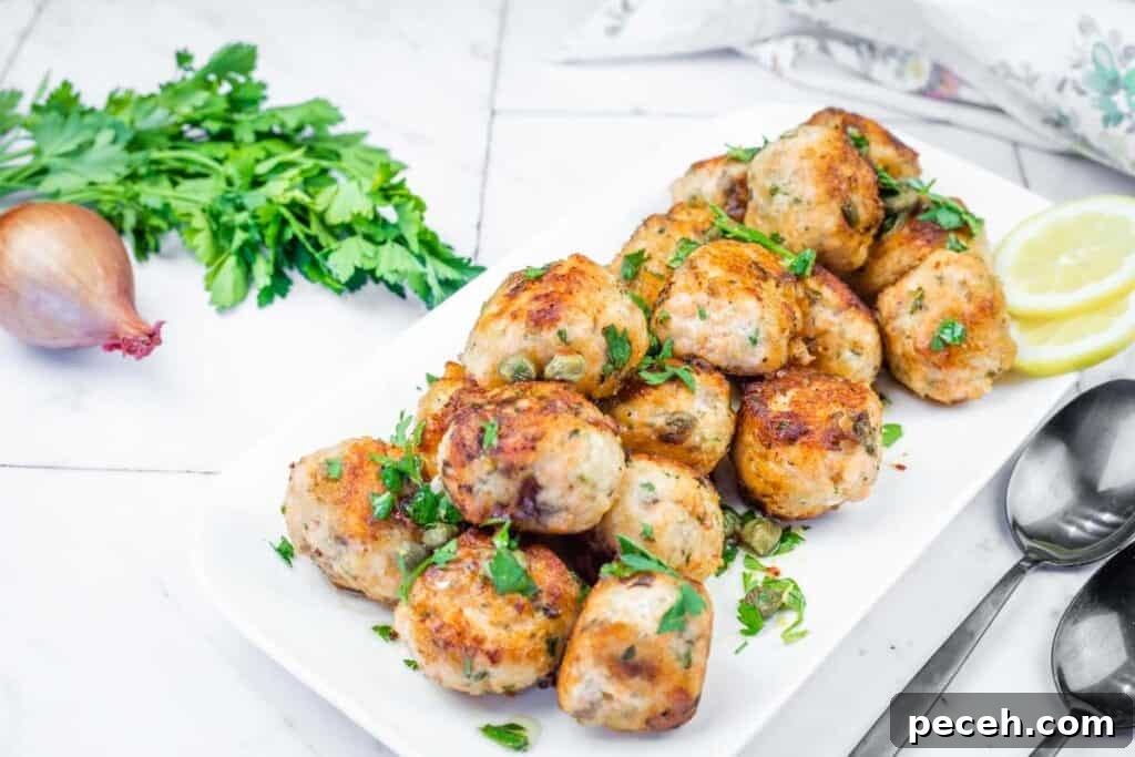 Crispy Pan-Fried Salmon Balls with Tangy Dill Sauce 15 A white platter filled with golden-brown turkey meatballs, garnished with parsley and capers, served with lemon slices and spoons.