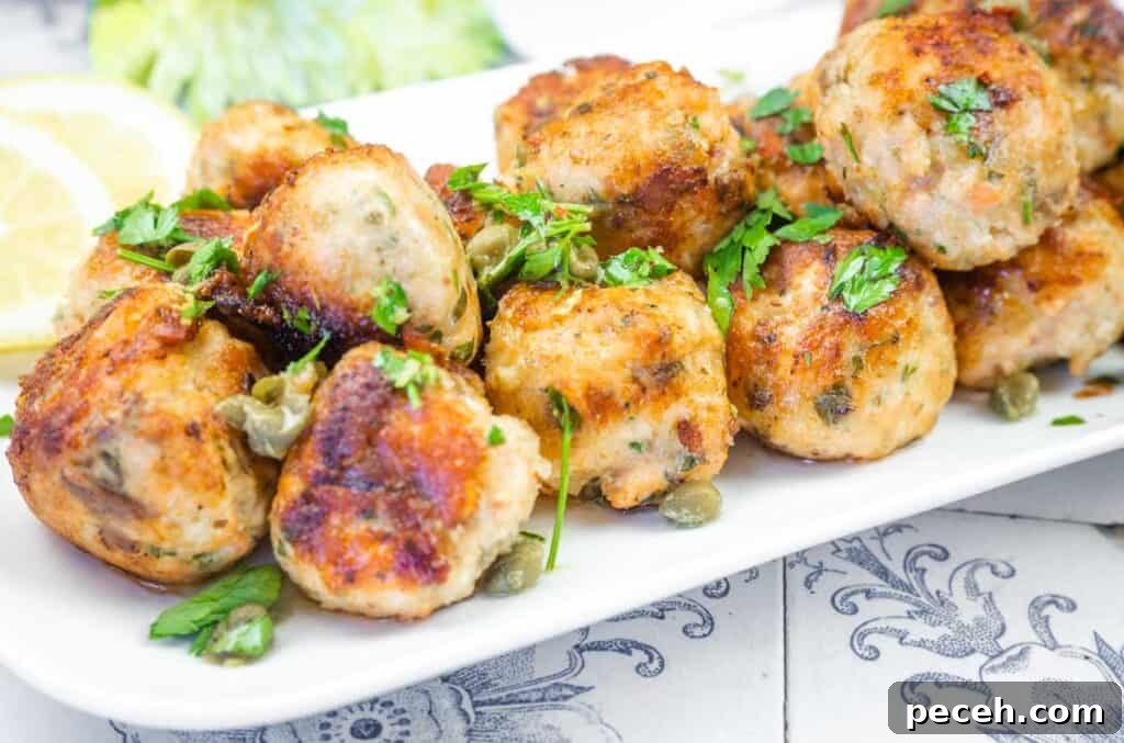 Crispy Pan-Fried Salmon Balls with Tangy Dill Sauce 3 A white platter filled with golden-brown turkey meatballs garnished with capers and fresh parsley, with lemon in the background.