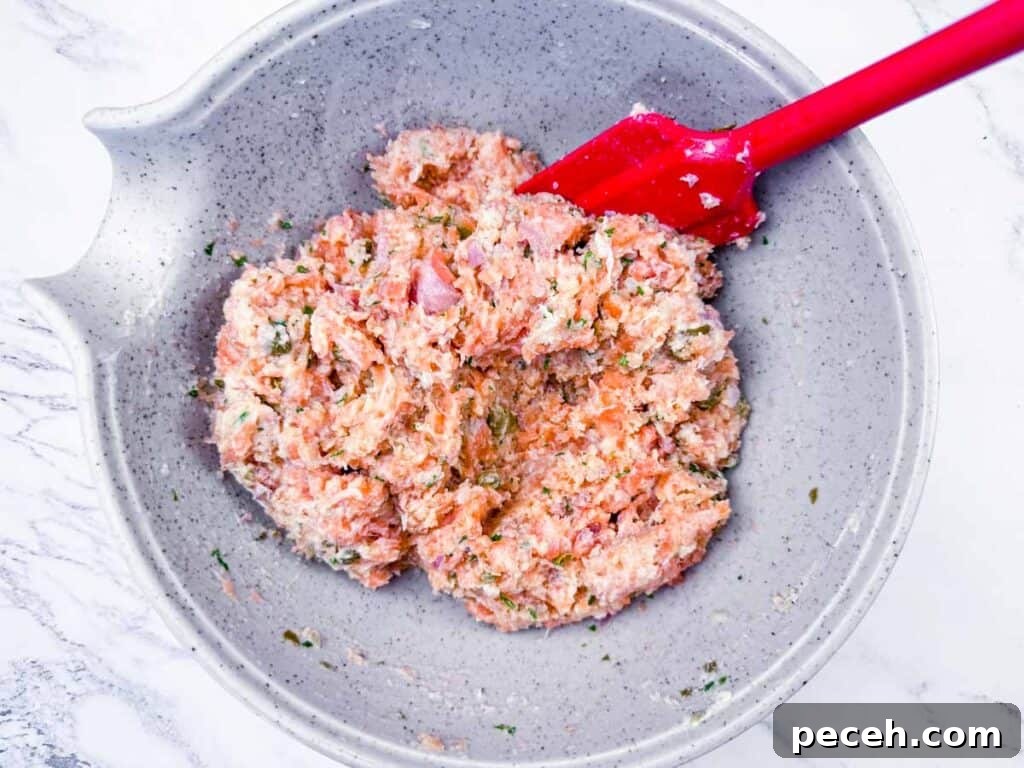 Crispy Pan-Fried Salmon Balls with Tangy Dill Sauce 9 Overhead shot of raw salmon mixture being stirred with a red spatula in a gray bowl.