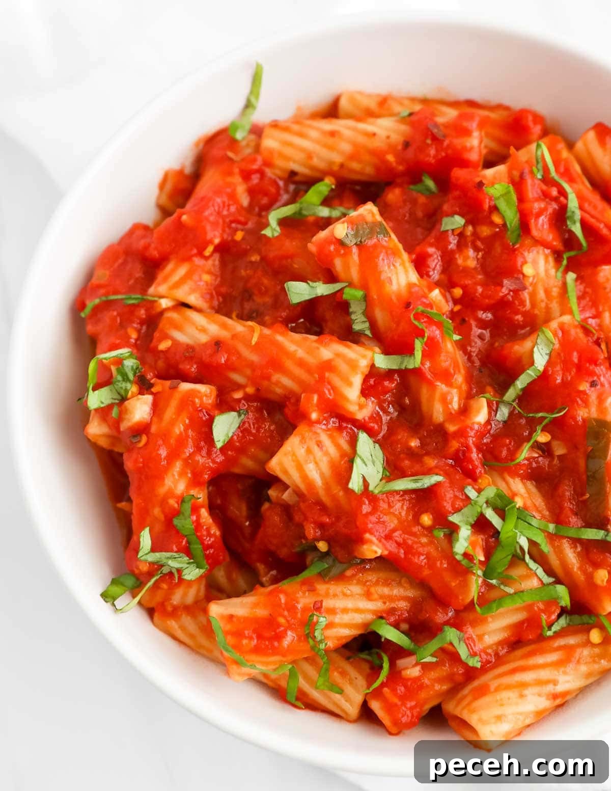 Spicy Rigatoni Arrabbiata with Garlic and Fresh Tomatoes 2 A close up picture of pasta in a red sauce that has chopped basil on top.