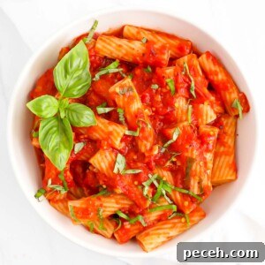 Spicy Rigatoni Arrabbiata with Garlic and Fresh Tomatoes 12 A white bowl filled with rigatoni covered in a red sauce and fresh basil.