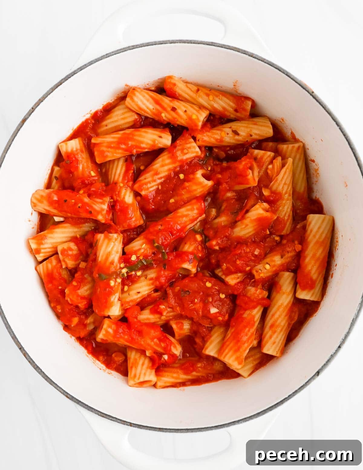 Spicy Rigatoni Arrabbiata with Garlic and Fresh Tomatoes 6 A large white pot filled with cooked pasta, red sauce, and crushed red pepper flakes.