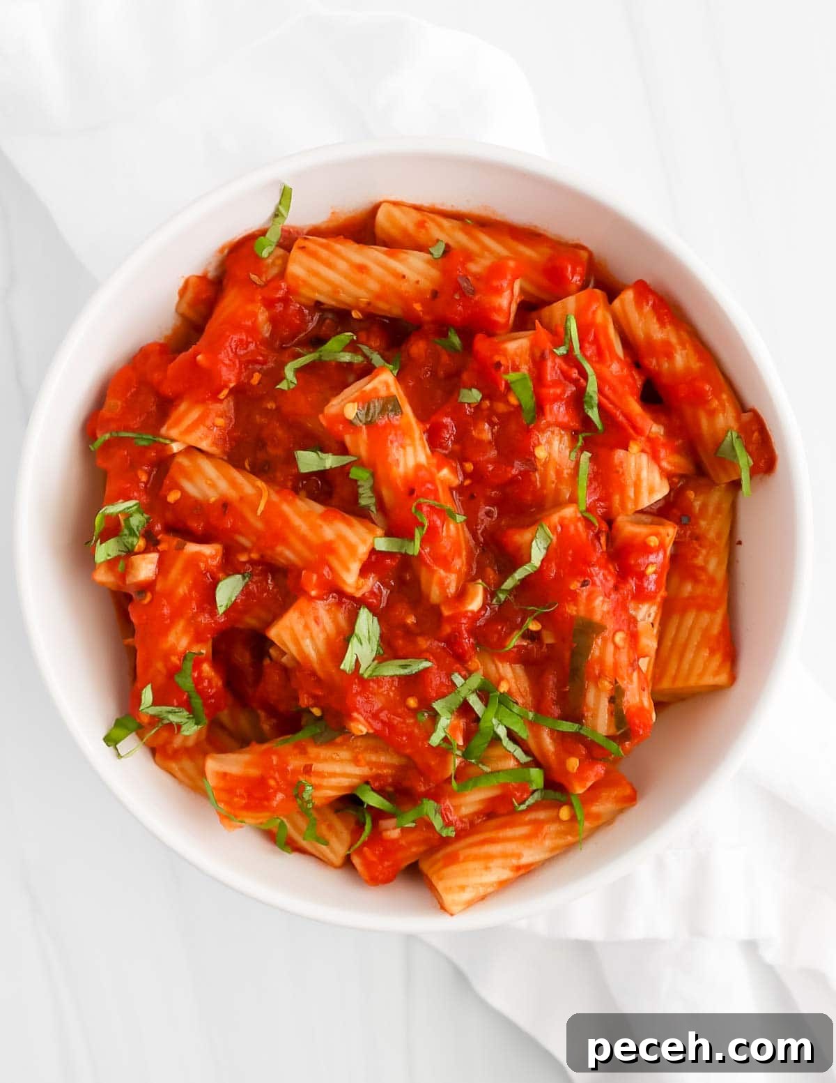 Spicy Rigatoni Arrabbiata with Garlic and Fresh Tomatoes 7 An overhead picture of a white bowl filled with cooked pasta that is covered in a red tomato sauce and has fresh green basil on top.