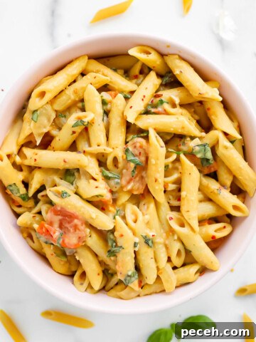 A pink bowl filled with penne pasta and creamy sauce.