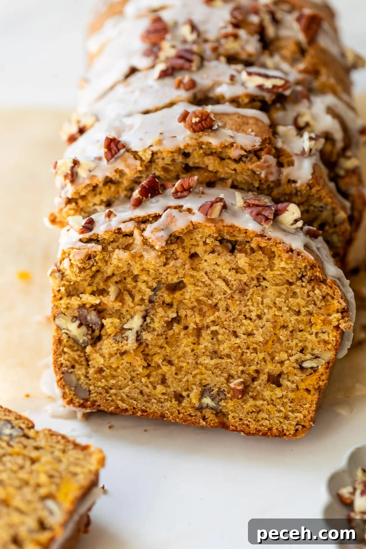 Moist Butternut Squash Loaf Recipe for Fall Baking 2 overhead view of a sliced loaf of butternut squash bread topped with a white glaze and pecans.