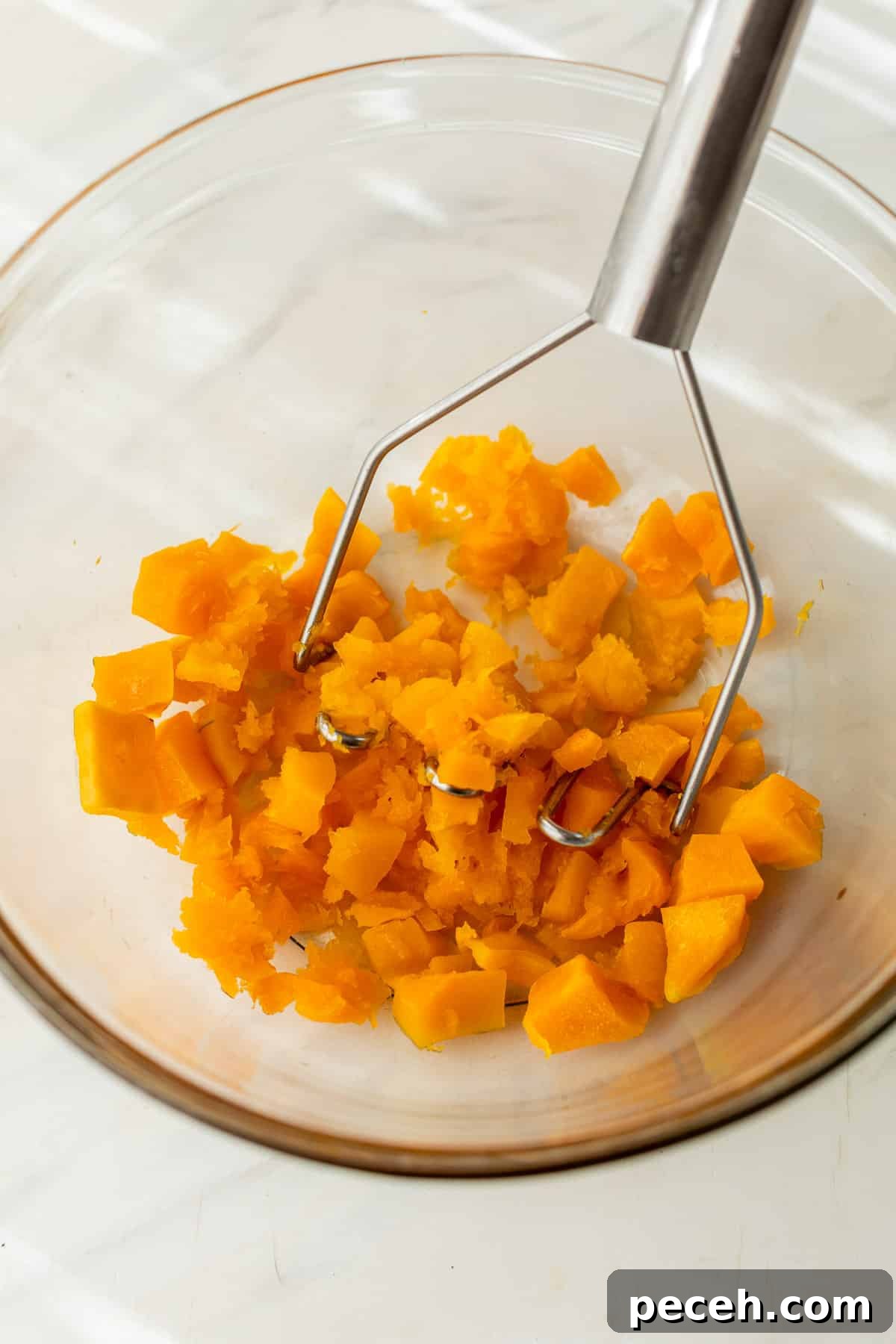 Moist Butternut Squash Loaf Recipe for Fall Baking 5 mashing butternut squash cubes in a glass bowl with a potato masher.
