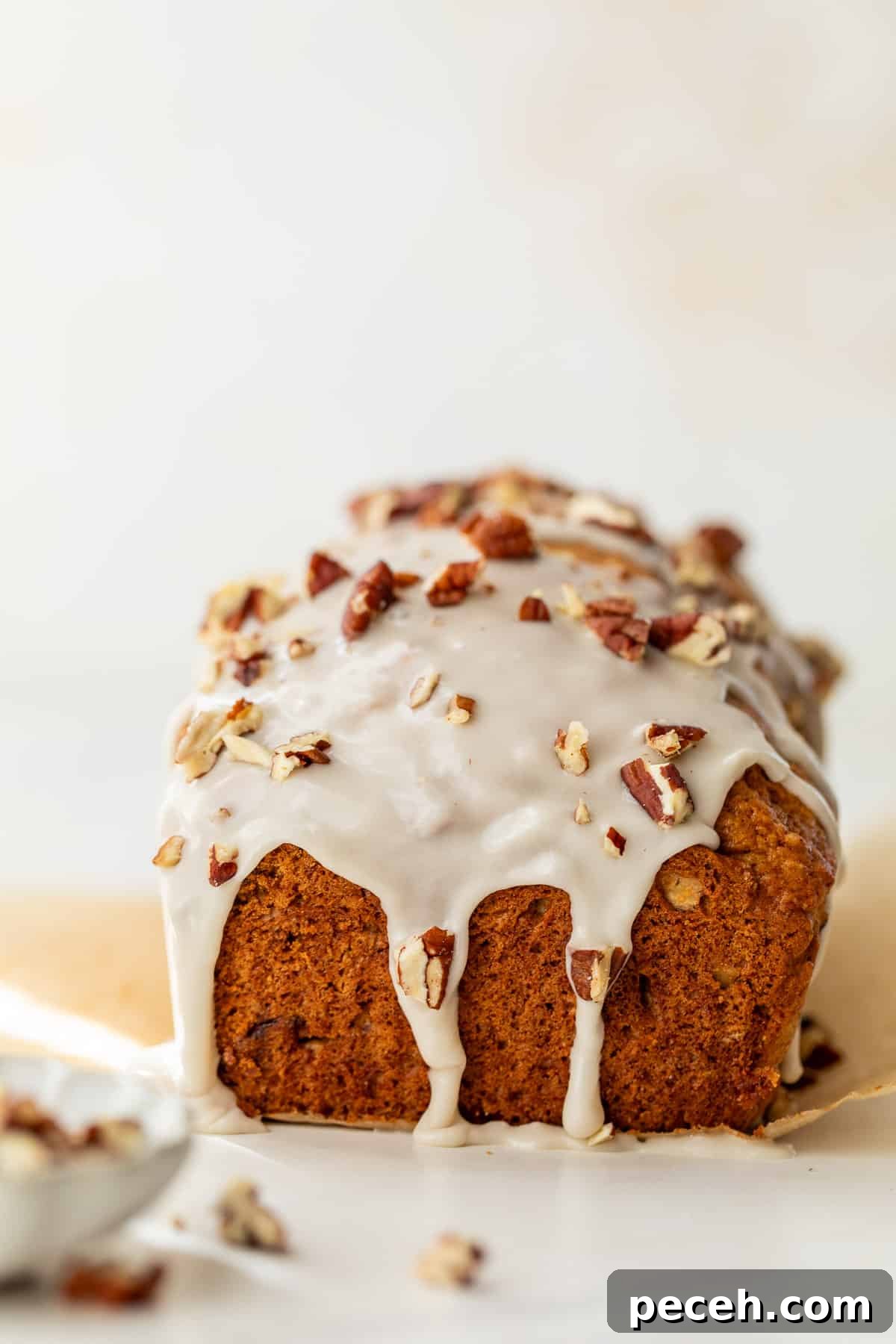 Moist Butternut Squash Loaf Recipe for Fall Baking 9 side view of a baked loaf of butternut squash bread topped with a white glaze and pecans.