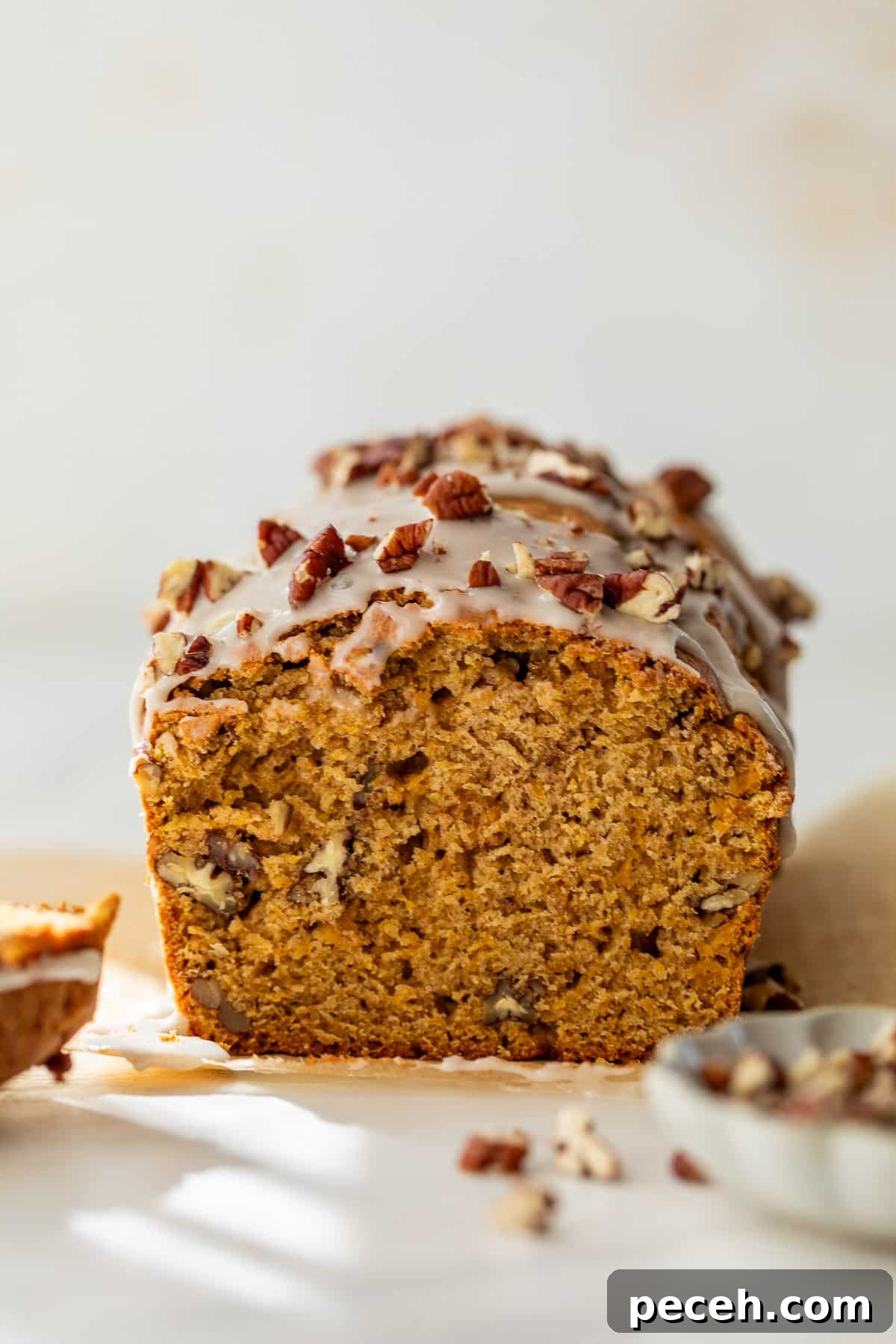 Moist Butternut Squash Loaf Recipe for Fall Baking 10 side view of a sliced loaf of butternut squash bread topped with a white glaze and pecans.