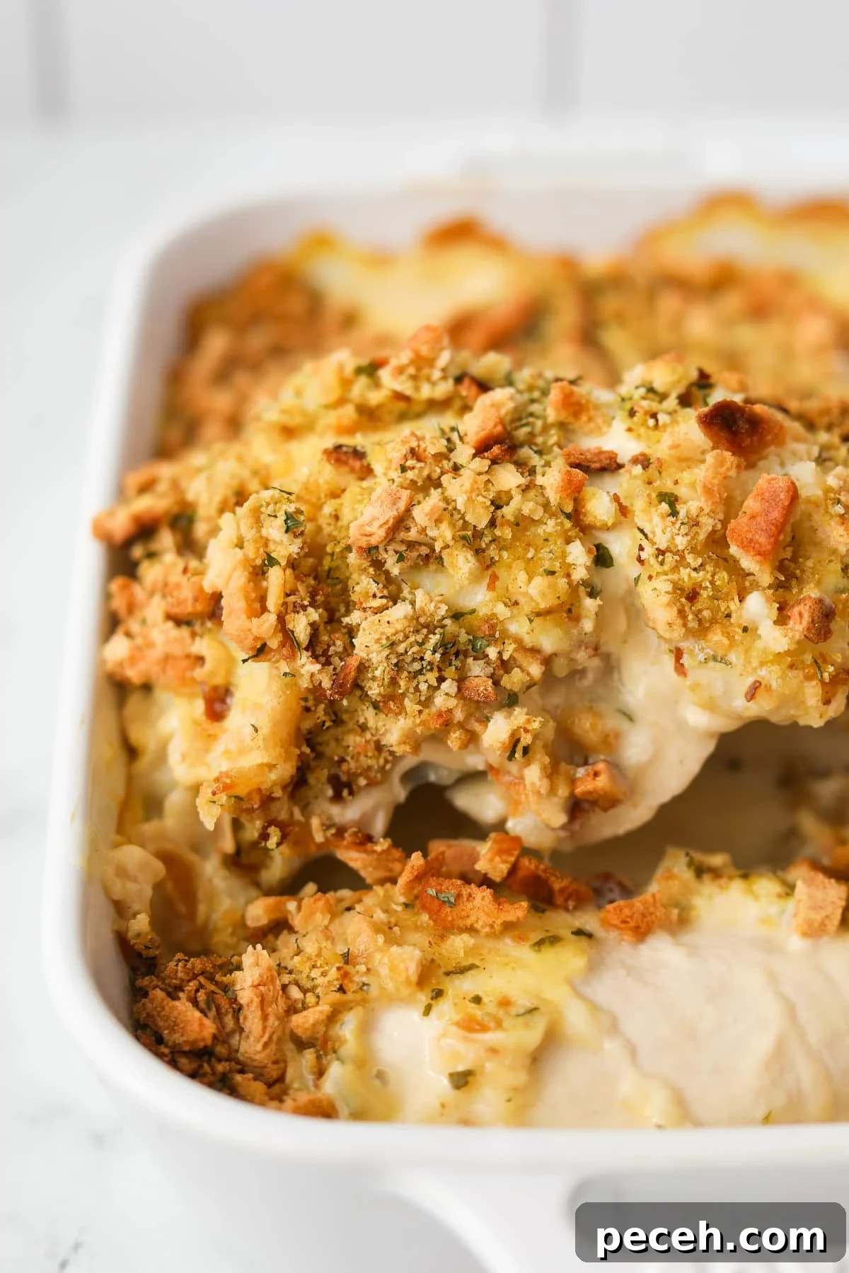 Creamy Swiss-Style Chicken Casserole with Mushrooms and Cheese 2 Lifting a chicken breast topped with stuffing mix from a baking dish.