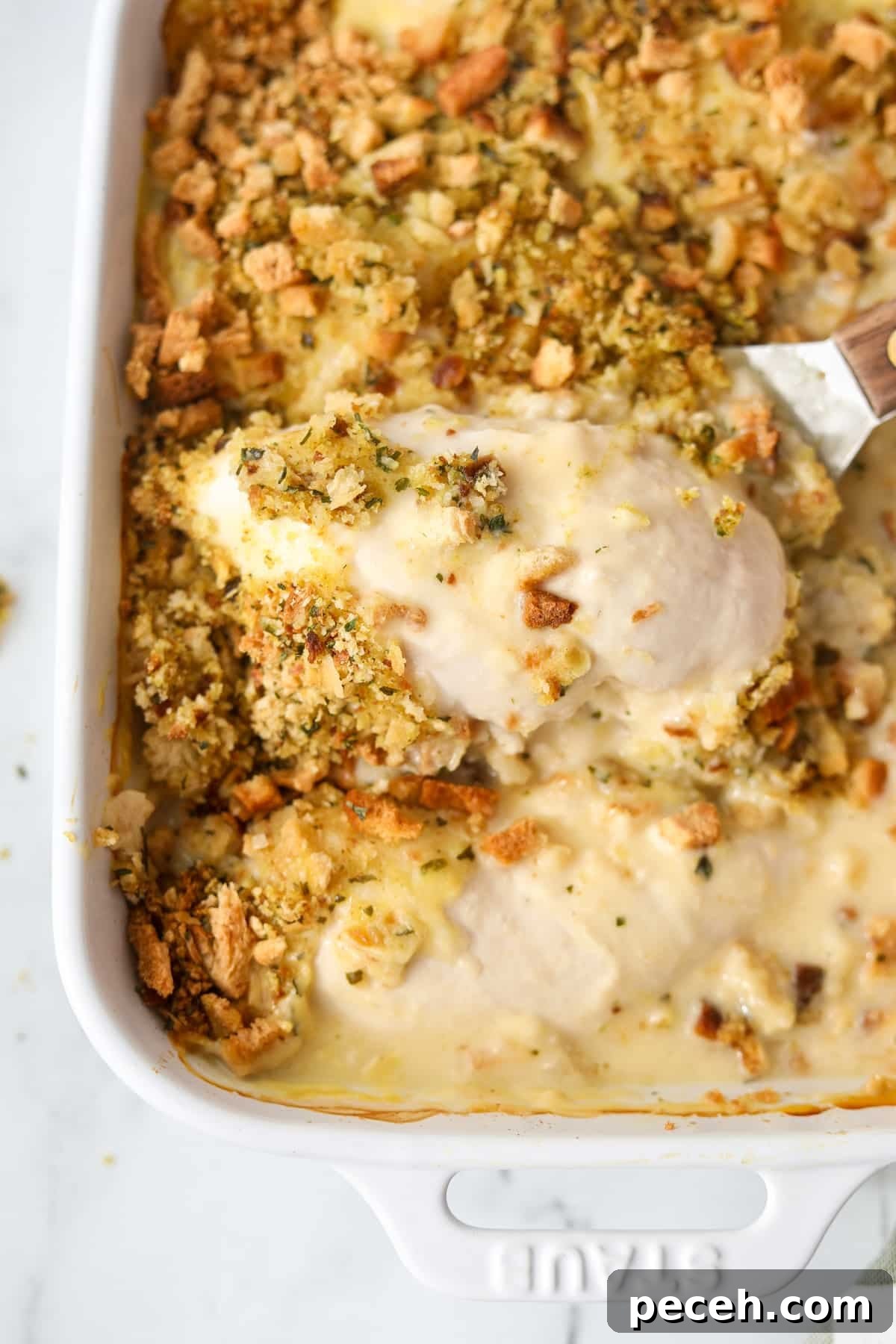 Creamy Swiss-Style Chicken Casserole with Mushrooms and Cheese 16 Lifting a chicken breast from a baking dish.
