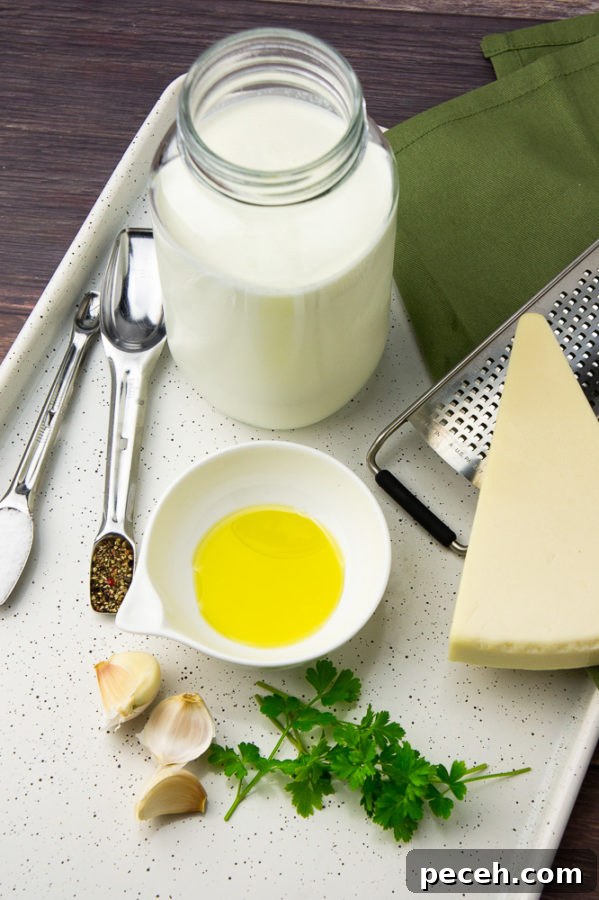 Creamy Asiago Sauce Recipe for Pasta and Vegetables 3 a jar of milk, wedge of asiago cheese, a bowl of oil, chopped parsley, and spices on a metal baking sheet