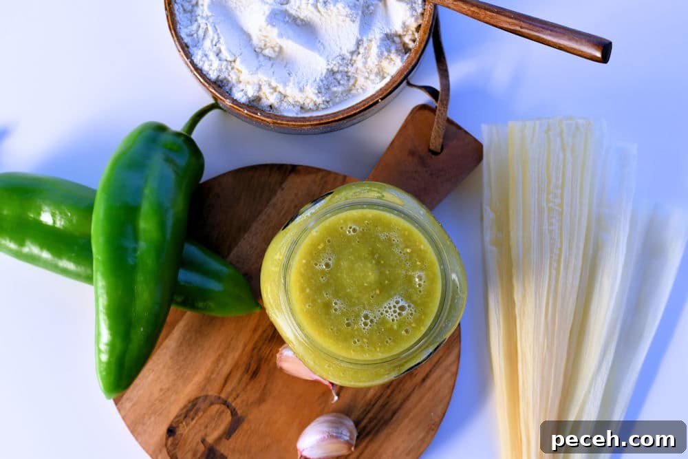 green tamale sauce in a jar shown on a counter with anaheim chiles and corn husks.