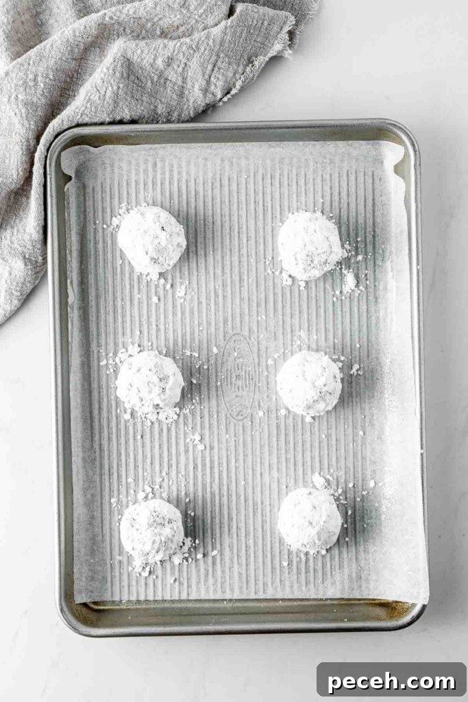 Fudgy Chocolate Crinkle Cookies Recipe 8 Chocolate cookie dough balls coated in powdered sugar on a baking tray.