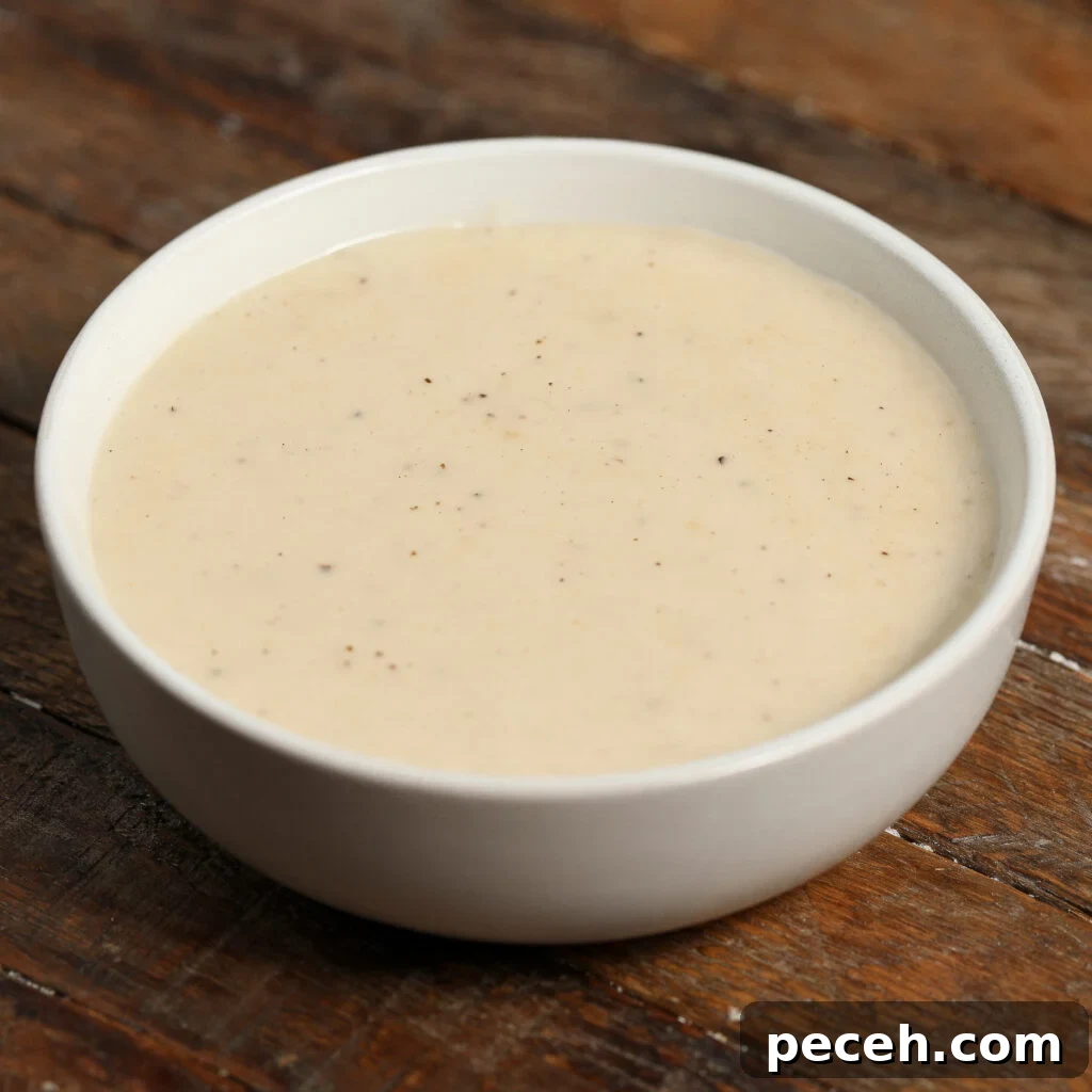 Roasted Garlic Parmesan Cream Sauce for Pasta 2 A white bowl filled with Roasted Garlic Parmesan Cream Sauce, creamy and lightly speckled with black pepper, sits on a rustic wooden surface.