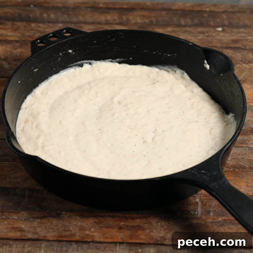 Roasted Garlic Parmesan Cream Sauce for Pasta 3 A cast iron skillet filled with Roasted Garlic Parmesan Cream Sauce sits on a rustic wooden surface. The sauce appears smooth and thick, with visible specks of seasoning.