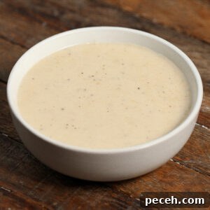 Roasted Garlic Parmesan Cream Sauce for Pasta 4 A white bowl filled with Roasted Garlic Parmesan Cream Sauce, creamy and lightly speckled with black pepper, sits on a rustic wooden surface.