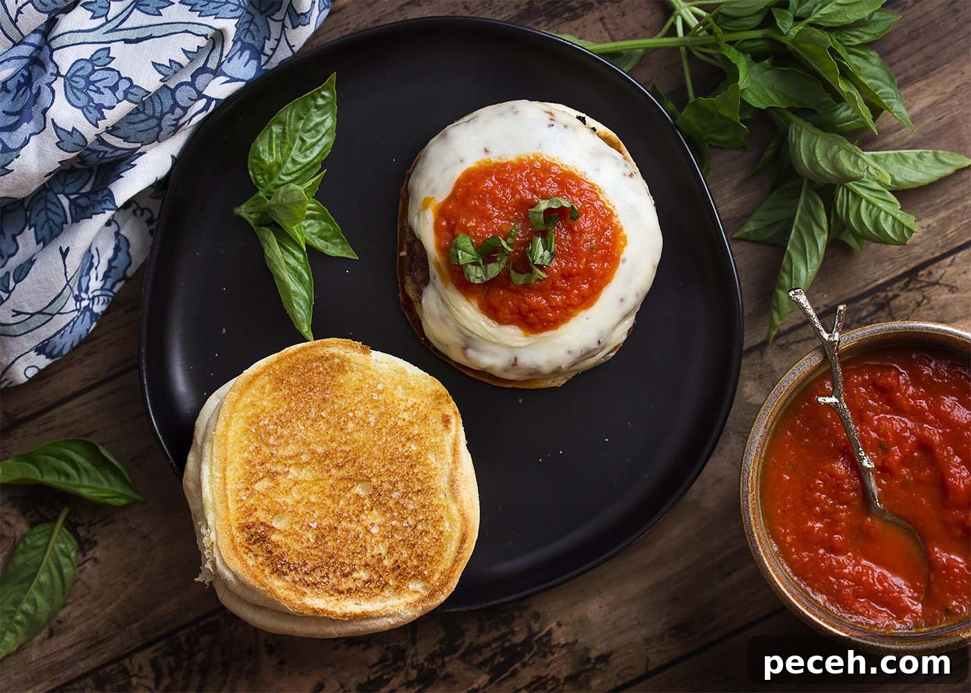 Open chicken parmesan burger showing crispy coating and melted cheese. Top view of a black plate with a burger open showing the crispy bun and melted cheese.