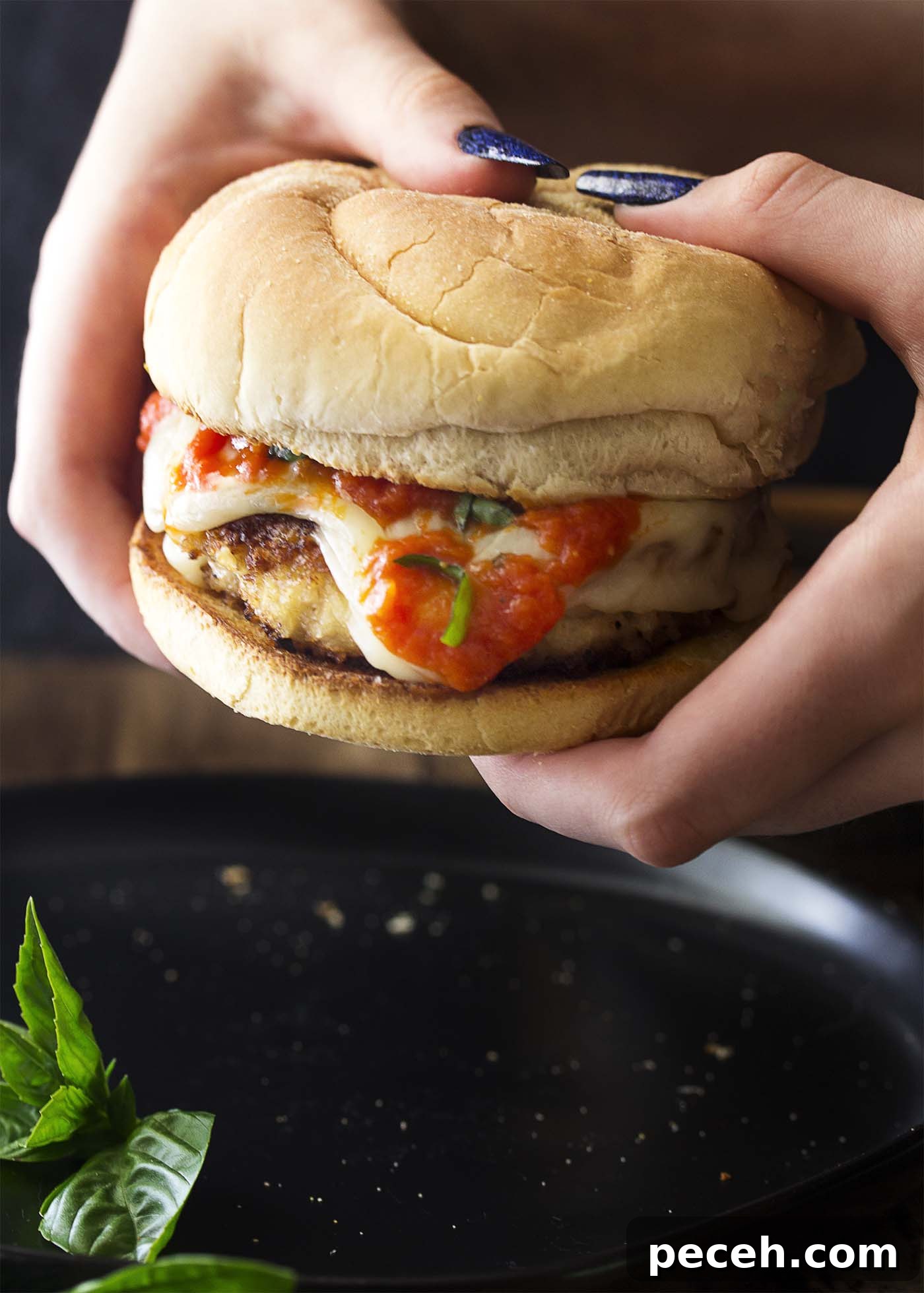 Two hands holding a chicken parmesan burger. Two hands holding a crispy chicken burger over a plate.