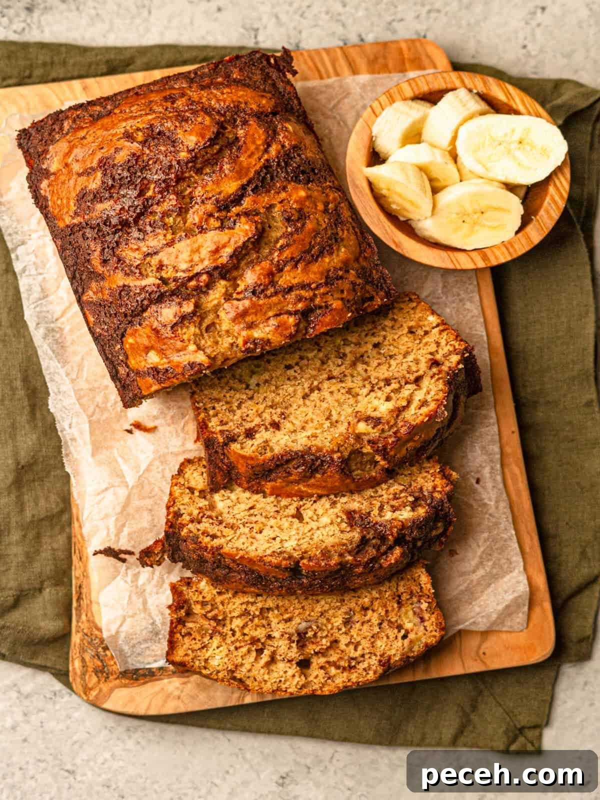 A marbled banana bread loaf with slices cut out next to a small bowl of banana slices.