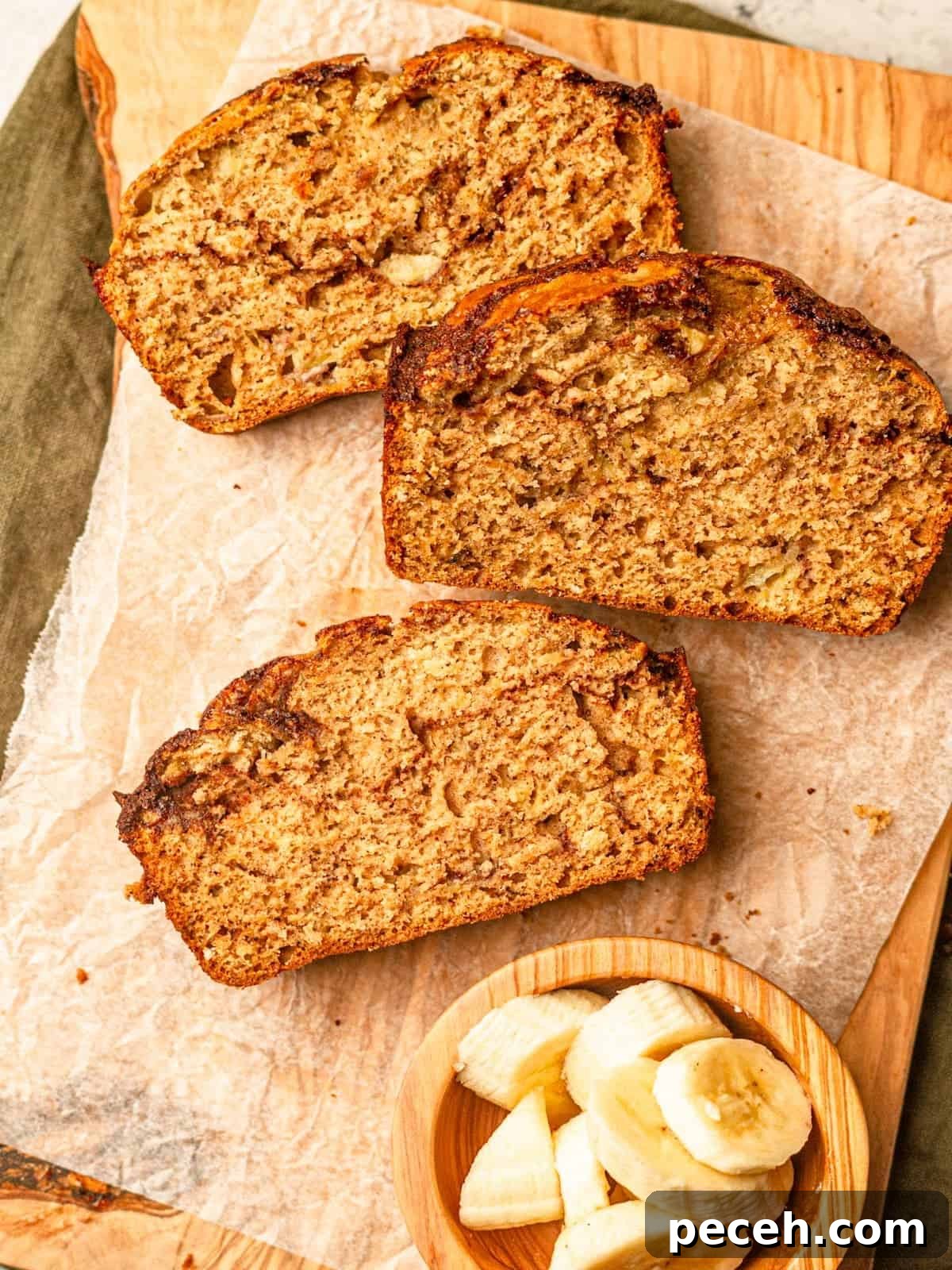 Three slices of banana bread on parchment paper on a cutting board.