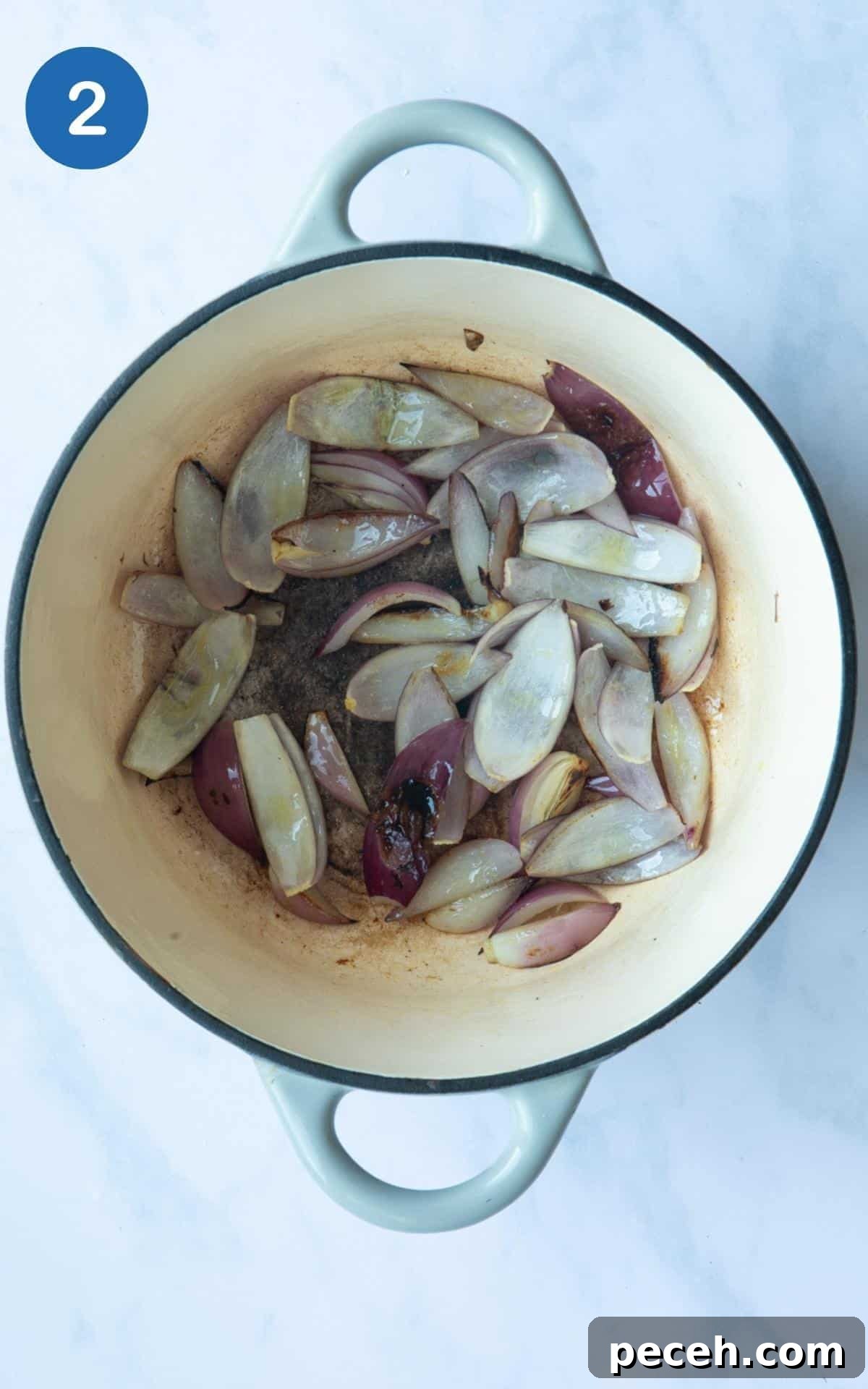 Creamy Sweet Potato Satay Curry with Coconut & Lime 5 Chopped onions in a large pot, that have been cooked until they have slightly browned/charred. Displayed on a white marble background.