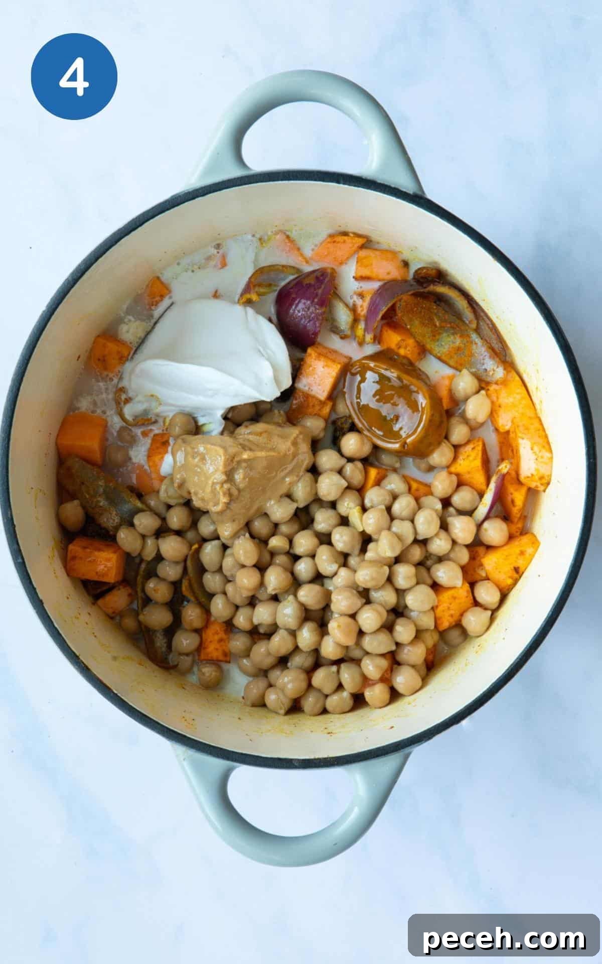 Creamy Sweet Potato Satay Curry with Coconut & Lime 7 large pot displayed on white marble background with uncooked chickpeas, cubed sweet potato and onion, dollop of coconut milk, vegetable stock cube and peanut butter.