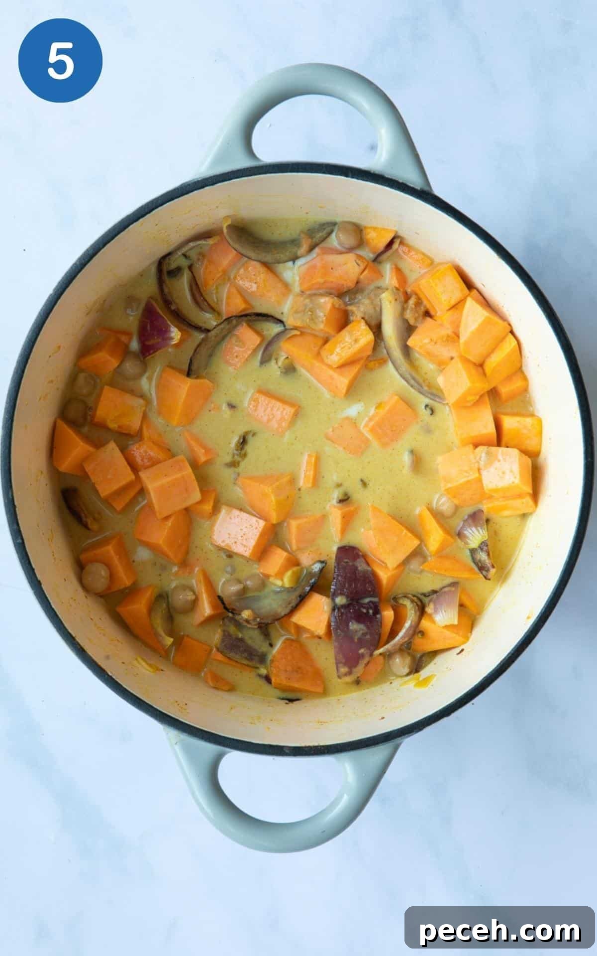 Creamy Sweet Potato Satay Curry with Coconut & Lime 8 Simmering ingredients in a large pot. Pot is displayed on white marble background.