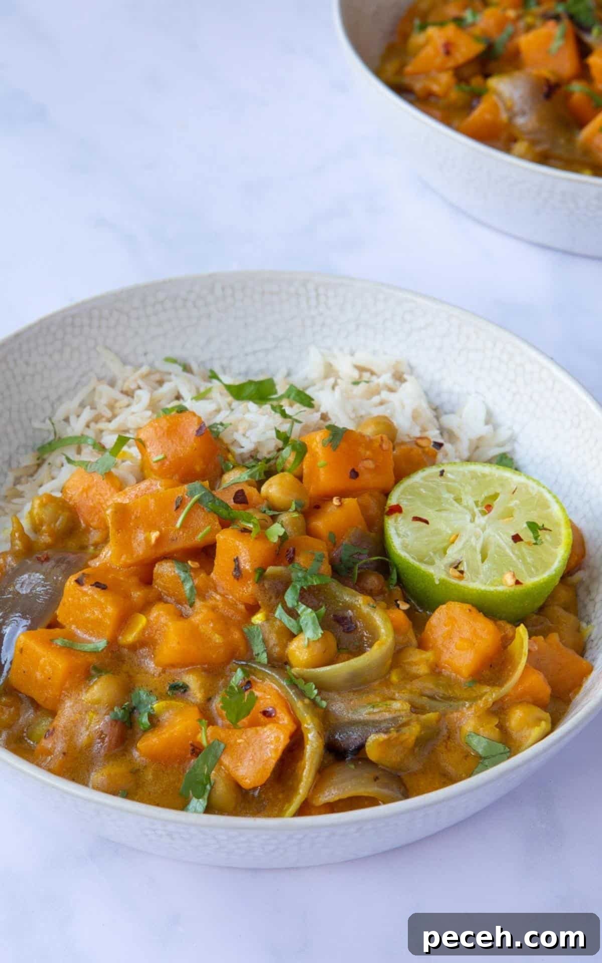 Creamy Sweet Potato Satay Curry with Coconut & Lime 9 Sweet Potato Satay Curry served in a bowl with rice, topped with coriander and lime wedges. Bowl is displayed on a white marble background.