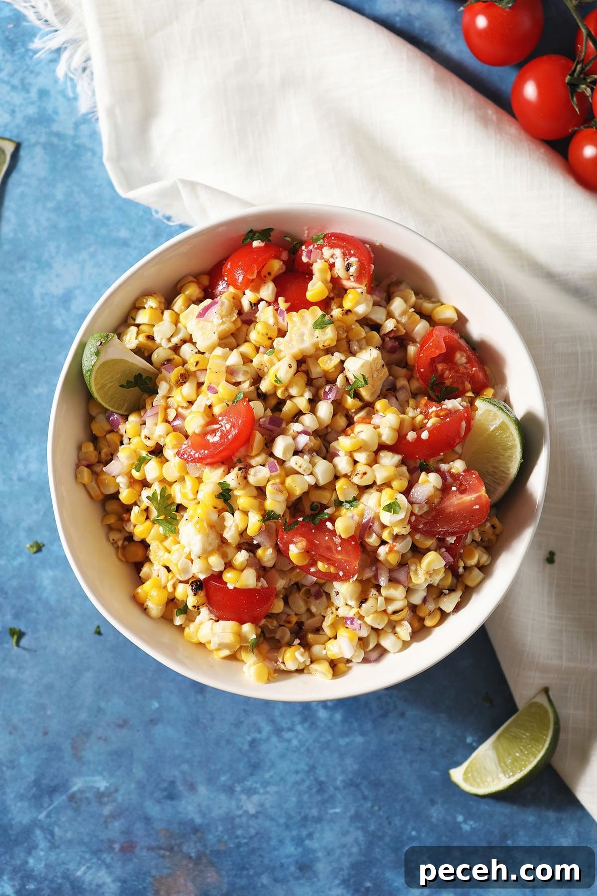 Smoky Charred Corn Salsa with Cilantro and Lime 6 A bowl of corn salsa with tomatoes and limes on a blue countertop