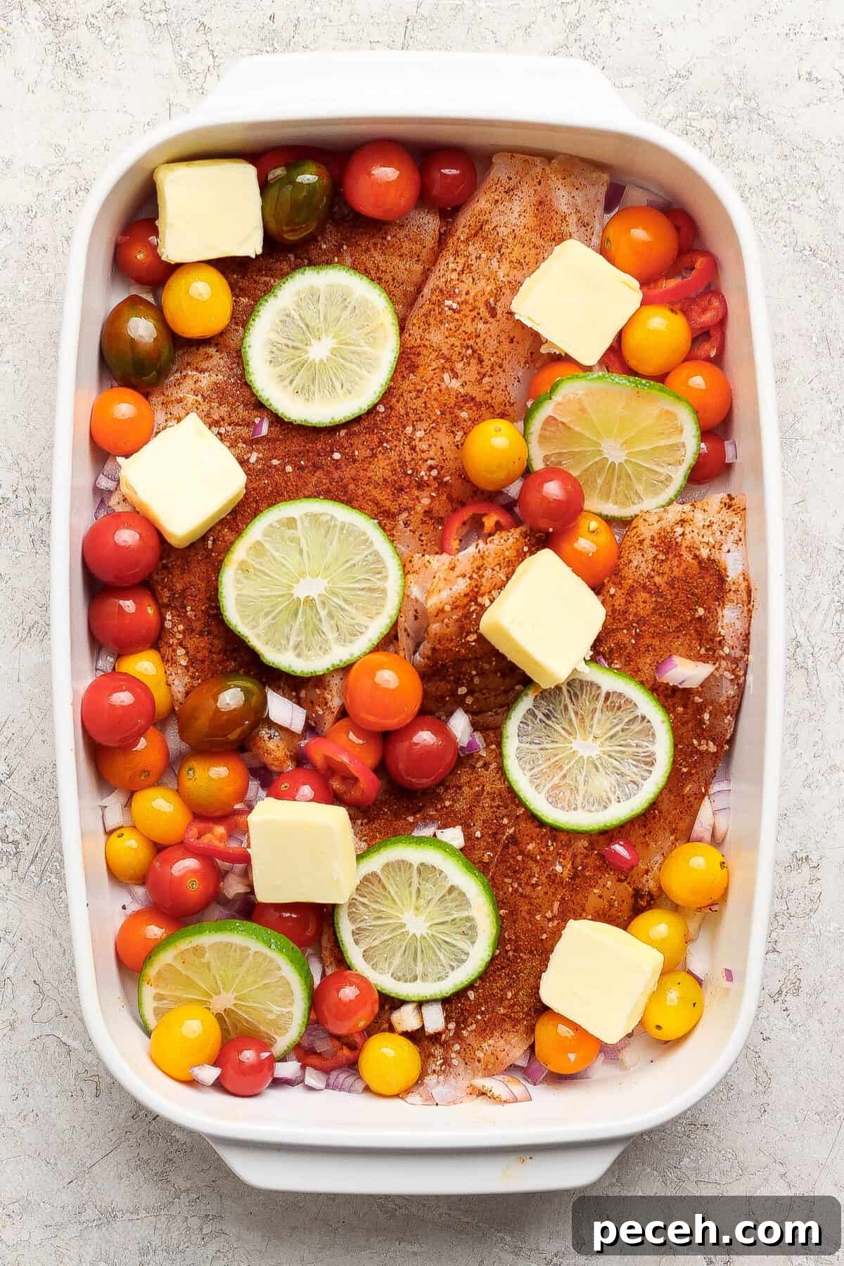 Baked Chile-Lime Fish Tacos with Tangy Cilantro Slaw 3 Raw seasoned fish fillets in a baking dish topped with lime slices, cherry tomatoes, onions, and butter cubes, ready for cooking.