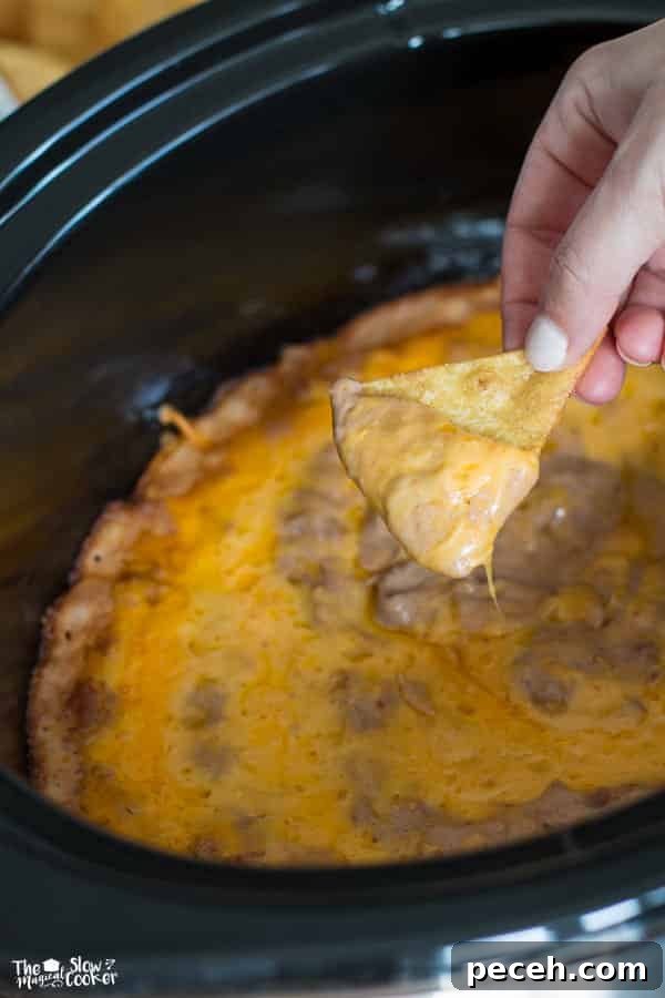 Creamy Bean and Cheese Dip for Parties 3 Dipping chip into bean dip in slow cooker.