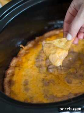 Creamy Bean and Cheese Dip for Parties 5 Creamy bean dip on chip in front of slow cooker.